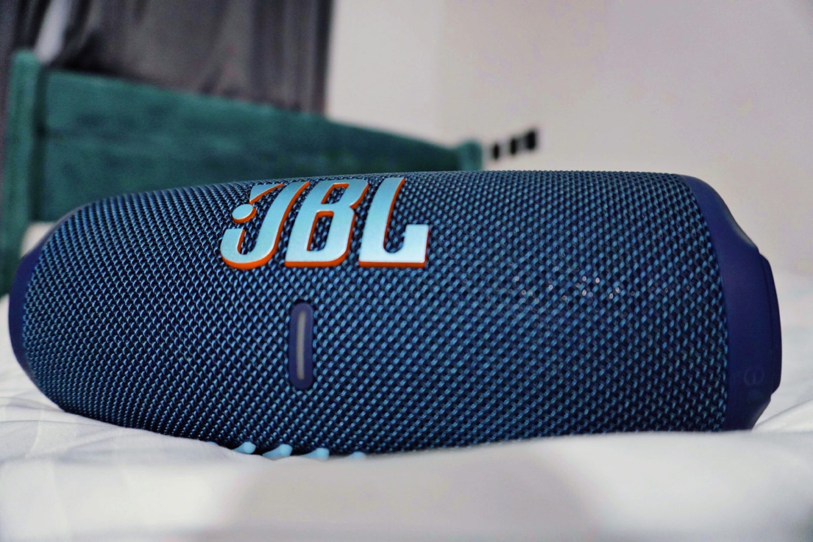 a blue jbl speaker laying on top of a bed